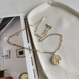 Close-up of a 925 sterling silver gold coin necklace on a textured ceramic dish