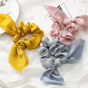 Detail of silk satin bow scrunchies in yellow, pink and blue colors on a white fabric