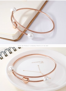 Detail of rose gold spiral wire bracelet with white pearl accents and heart charm