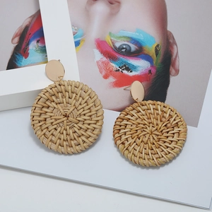 Gros plan de boucles d'oreilles rondes en rotin tressé avec clou doré sur fond blanc