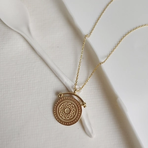 Detailed view of a gold-plated round embossed flower pendant on a dainty link chain