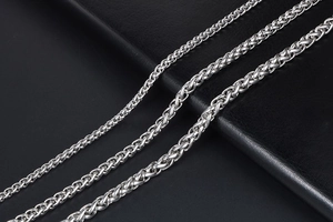 Detailed view of three polished stainless steel wheat link chains on dark leather
