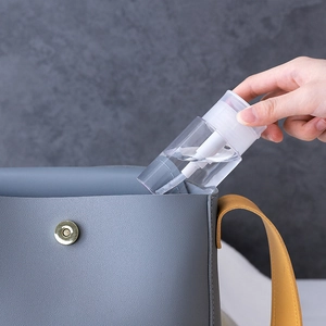 Clear plastic press bottle for makeup remover being placed into a gray leather bag