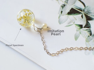 Detail of transparent resin pendant with golden dried flower and pearl on silver chain