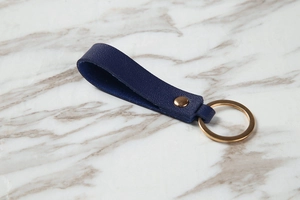 Close-up of dark blue leather keychain with litchi texture and gold metal ring