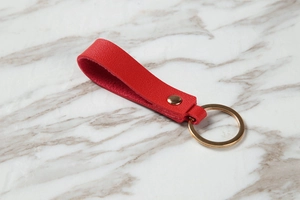 Detail of red lychee grain leather keychain with elegant gold metal ring and rivet