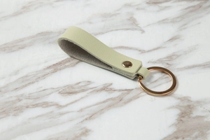 Close-up of light green textured leather keychain with elegant gold-tone metal ring