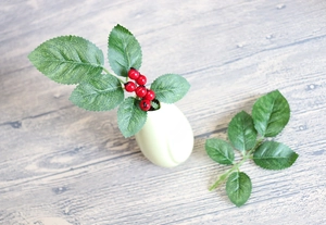 Close-up of artificial red berries and green leaves in a small light green ceramic vase