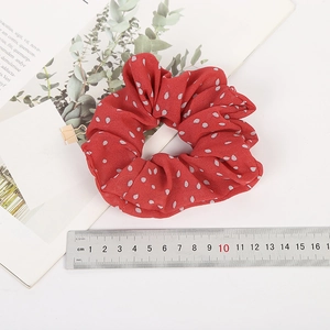 Detail view of red polka dot chiffon hair scrunchie with measuring ruler on white surface
