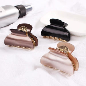 Three shell-shaped acrylic hair claws in brown, black, and nude colors with gold springs