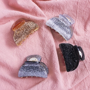 Close-up of four glitter acrylic shark hair clips in gold, silver, grey, and black colors