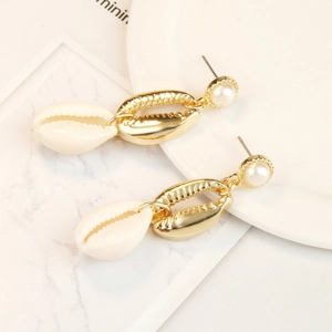 Close-up of bohemian gold shell earrings with white pearl detail on a marble surface