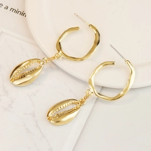 Macro shot of gold cowrie shell earrings with open metal rings on white ceramic