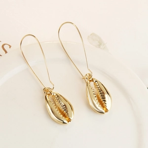 Close-up of golden shell earring with long hook on white ceramic tray