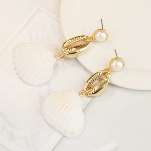Detail shot of pearl and gold seashell earrings on a white marble surface background