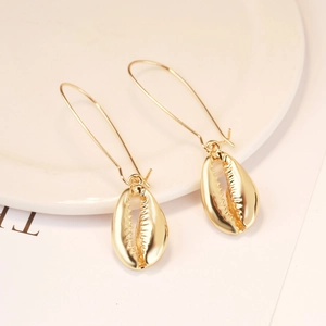 Detail of golden bohemian shell drop earrings on white ceramic dish for summer style