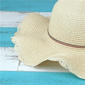 Detailed close-up of summer straw hat with wavy brim and striped ribbon decoration