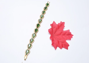 Gros plan d'un bracelet doré avec cristal vert en poire et décor de feuille rouge