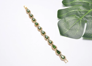 Détail d'un bracelet doré avec cristal goutte vert et petites pierres de zircon brillantes