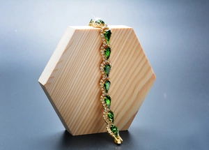 Détail d'un bracelet doré avec pierres gouttes vertes et diamants sur bois