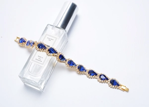 Détail d'un bracelet doré orné de pierres bleues posé sur un flacon de parfum