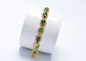 Détail d'un bracelet doré avec cristaux goutte d'eau verts sur un support d'exposition blanc