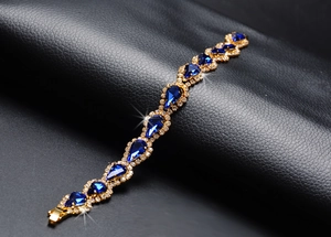 Détail d'un bracelet doré avec cristaux bleus en goutte et diamants sur cuir noir élégant