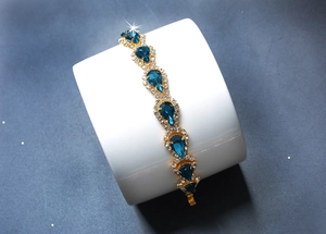 Détail d'un bracelet doré avec cristal bleu en goutte d'eau et strass étincelants