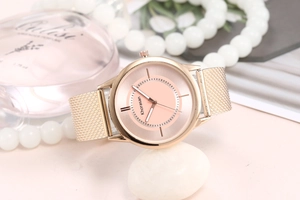 Detail of rose gold mesh strap watch with pink dial next to pearls and perfume bottle