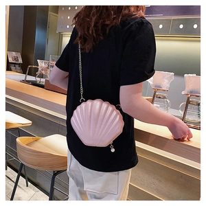 Detail showing pearl pink shell-shaped crossbody bag with gold chain on model's shoulder