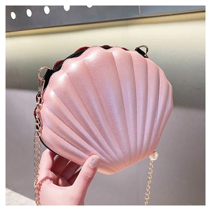Detail of pink shell crossbody bag with pearl charm and gold chain strap close-up