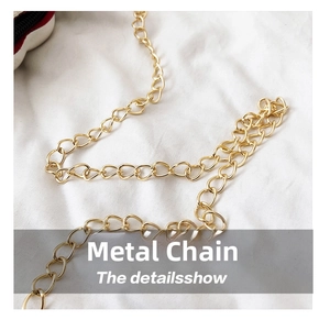 Detail of elegant gold-toned metal chain strap on textured white fabric background