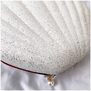 Close-up of white shell-shaped clutch with glitter finish and pearl zipper charm