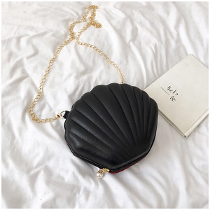 Close-up of black shell-shaped crossbody bag with gold chain and white pearl zipper charm