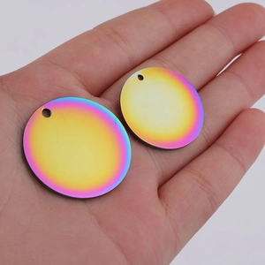 Close-up of rainbow gradient stainless steel round pendants held in palm showing size