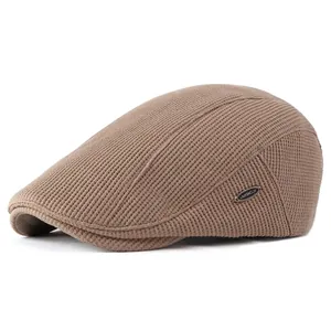 Dark brown waffle knit newsboy cap with premium metal logo detail in minimalist style