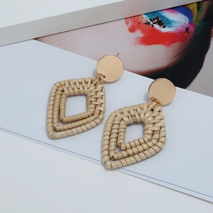 Détail de boucles d'oreilles bohèmes en rotin tressé à la main avec clou doré géométrique