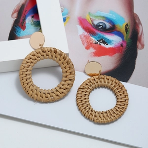 Détail de boucles d'oreilles rondes en rotin tressé avec clous dorés sur fond artistique