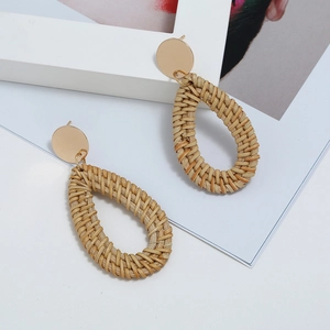 Détail de boucles d'oreilles artisanales en rotin tressé et clous dorés chic