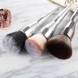 Three professional large powder brushes with silver metallic handles on marble surface