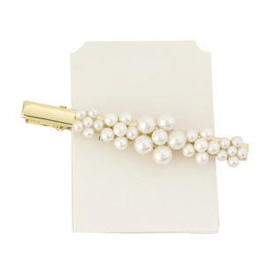 Detailed view of artificial white pearls on a gold-tone metal alligator hair clip
