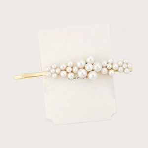 Detailed view of pearl hair clip with gold metal frame on white display card