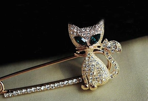 Detailed close-up of a gold cat brooch featuring green gemstone eyes and clear rhinestones