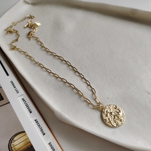 Detailed macro view of a vintage gold coin pendant on a textured ceramic dish