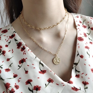 Detail of layered gold coin necklace set on model with vintage embossed pendant