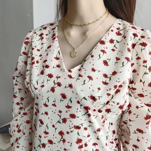 Close-up of layered gold coin necklaces on a model wearing a floral V-neck top