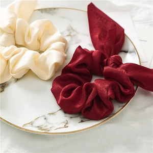 Detail of premium cream and burgundy satin silk scrunchies on a marble plate