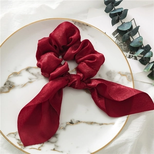 Detailed view of burgundy satin scrunchie with rabbit ear bow on a marble tray