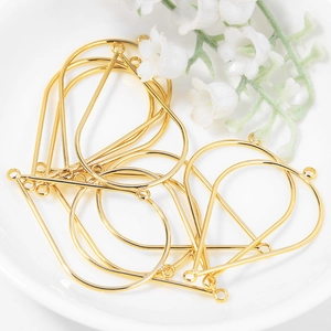 Golden teardrop metal frame pendants for DIY jewelry making on white ceramic plate