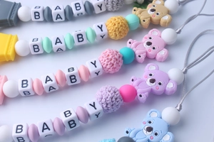 Detail of five silicone baby pacifier clips with koala teethers and BABY letter beads
